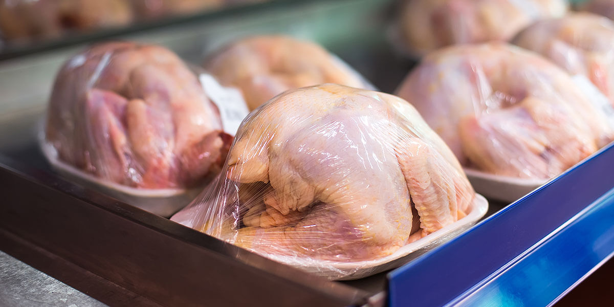 Multiple whole chicken carcasses wrapped in plastic on a table.